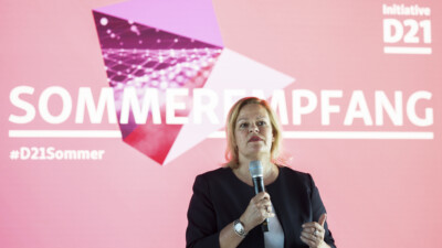 Bundesinnenministerin steht mit einem Mikrofon vor einer LED-Wand, auf der eine Slide mit dem Titel "Sommerempfang der Initiative D21" zu sehen ist.