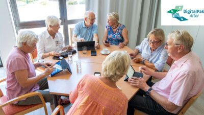 Ältere Menschen sitzen um einen runden Tisch und beschäftigen sich mit digitalen Geräten.