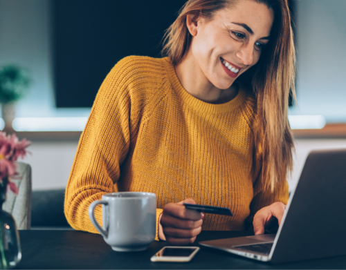 Eine Frau mit einem Personalausweis vor ihrem Laptop. Außerdem stehen ein Kaffee und ein Smartphone bereit.