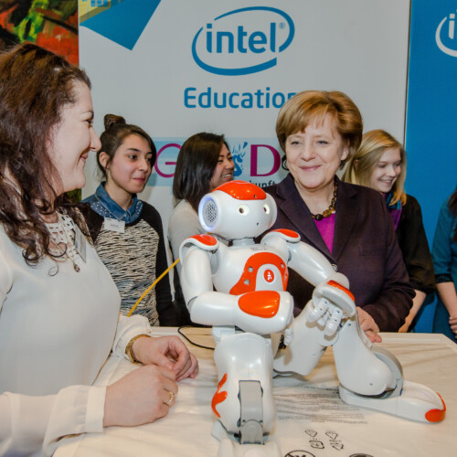 Ein Roboter sitzt gemütlich auf einem Tisch vor Angela Merkel und Schülerinnen beim Girls'Day-Auftakt