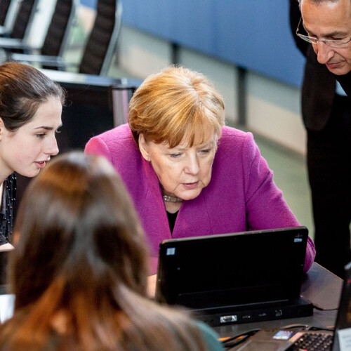Angela Merkel und eine Schülerin sowie Hannes Schwaderer gucken interessiert auf einen Laptop beim Girls'Day-Auftakt im Bundeskanzleramt
