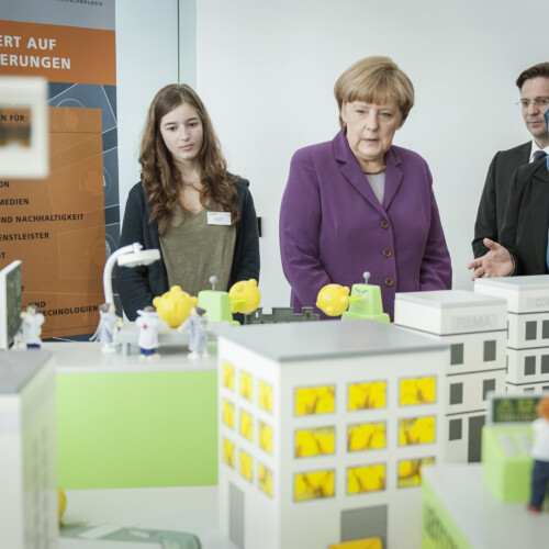 Angela Merkel und zwei Schülerinnen vor einem Modell einer Stadt der Zukunft beim Girls'Day-Auftakt.