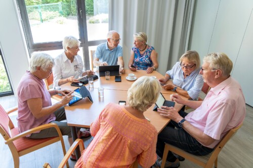 Mehrere Senior*innen sitzen um einen runden Tisch und beschäftigen sich gemeinsam mit digitalen Geräten
