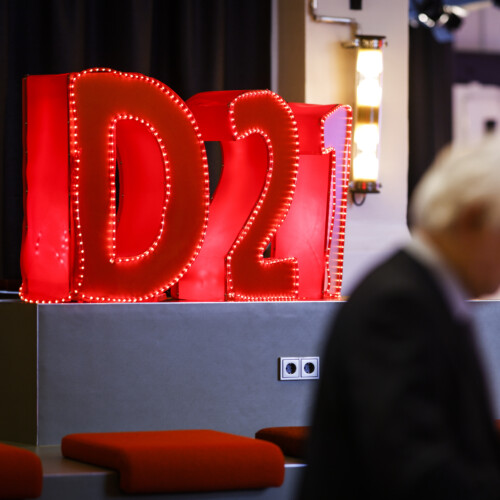 Große rote D21-Buchstaben sind beleuchtet im Hintergrund. Davor liest eine unscharfe Person in etwas.
