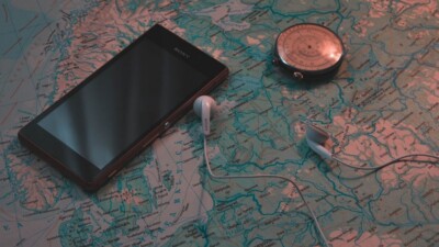 Eine Landkarte, auf der ein Handy, ein Kompass und ein paar In-Ear-Kopfhörer liegen.