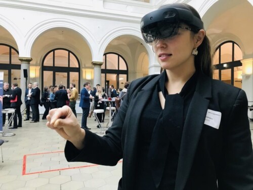 Eine Frau trägt eine HoloLens (Mixed Reality Brille) im Gesicht und gestikuliert dabei mit ihrer rechten Hand.