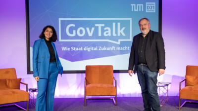Tatiana Muñoz und Franz-Reinhard Habbel vor einem Panel mit dem Text: "GovTalk. Wie Staat digital Zukunft macht"