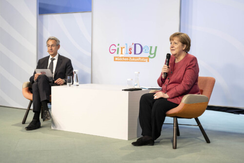Angela Merkel und Hannes Schwaderer begrüßen die Schülerinnen im Livestream, die ins Kanzleramt geschaltet werden.