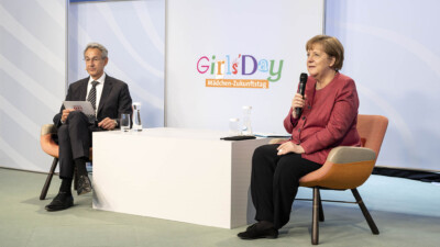 Angela Merkel und Hannes Schwaderer begrüßen die Schülerinnen im Livestream, die ins Kanzleramt geschaltet werden.
