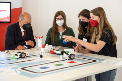 Drei Schüler*innen erkunden gemeinsam mit Bundeskanzler Scholz den Miniatur-Aufbau einer Smart Factory