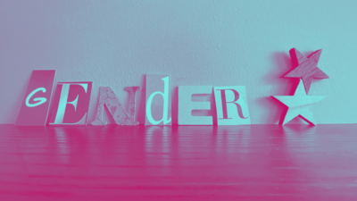 Die Buchstaben G E N D E R und ein Sternchen stehen als Holzfiguren auf einem Tisch. Das Bild ist mit einem pink-türkisen Farbverlauf-Filter versehen.