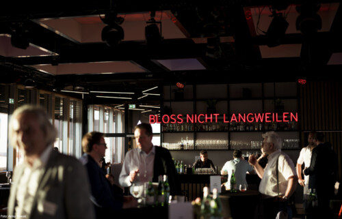 Eine athmosphärische Aufnahme der Bar über der ein Neonschriftzug mit den Worten "BLOSS NICHT LANGWEILEN" in Großbuchstaben hängt