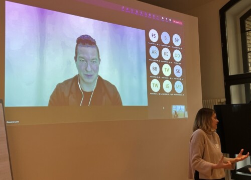 Mit dem Beamer wird eine Microsoft-Teams-Videokonferenz an die Wand geworfen, eine Person hält darüber gerade einen Vortrag.