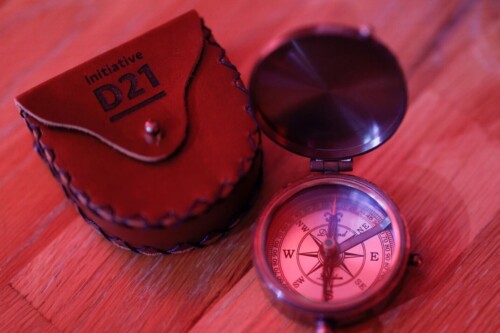 Ein Kompass neben einer mit dem D21-Logo gravierten Ledertasche.