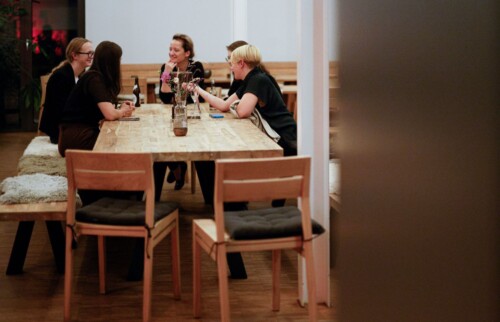 An einem Tisch sitzen mehrere Personen und stecken zum Gespräch die Köpfe zusammen.
