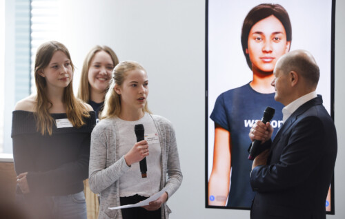 Zwei Schülerinnen im Gespräch mit dem Bundeskanzler. Im Hintergrund ein Hochkant-Bildschirm, der einen Avatar zeigt.