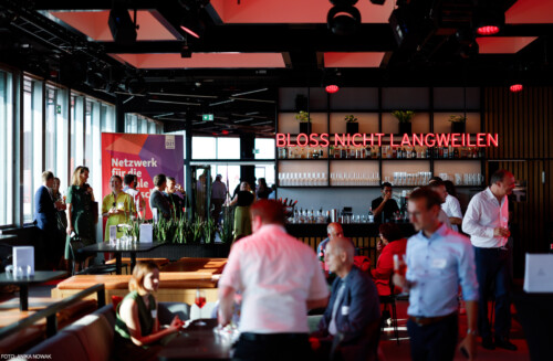 Über der Bar im gefüllten Raum strahlt in roten Lichtbuchstaben der Schriftzug "Bloss nicht langweilen"