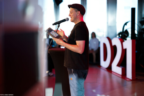 Sebastian 23 auf der Bühne beim Lesen am Mikrofon. Im Hintergrund die großen leuchtenden D21-Buchstaben