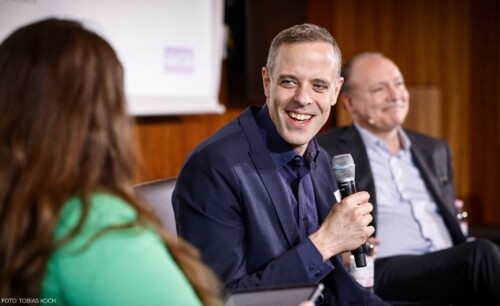 Ein Bild, auf dem Dr. Markus Richter, CIO des Bundes und Marc Reinhardt, Präsident der Initiative D21, gemeinsam mit der Moderatorin auf der Bühne diskutieren.