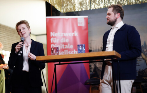 Anne-Marie Tumescheit und Jan Quaing mit Mikrofonen hinter einem Stehtisch auf der Bühne