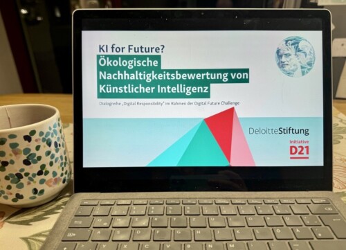 Auf einem Laptop wird die Präsentation des Events "KI for Future" angezeigt. Daneben steht eine Tasse.