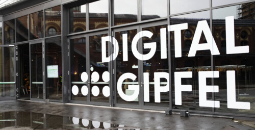 Auf der Glasfront der Location des Digital-Gipfel 2022 ist der Slogan "Digitalgipfel" in weißen Klebebuchstaben angebracht.