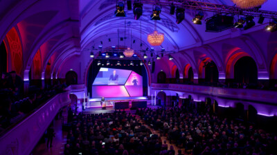 EIn großer Saal mit Bühne, in dem alles in pink-lilanem Licht gehalten ist